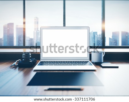 Generic laptop on the workspace with panoramic windows.  City at sunrise in a background. 3D rendering