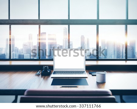 Photo of laptop on the worksplace with panoramic windows.  City at sunrise in a background. 3D rendering