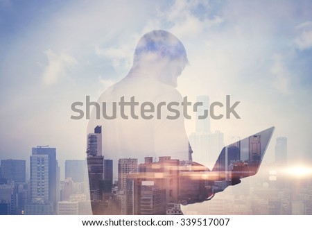 Double exposure of man with laptop and contemporary city on the background. Horizontal