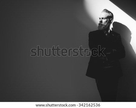 Stylish bearded man wearing trendy suit, stands against a wall  and looking on  left side of the frame