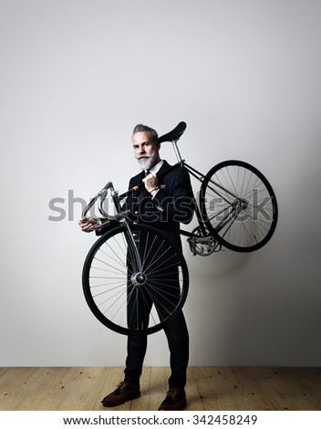 Portrait of a handsome middle aged man wearing suit and holding his classic bicycle on the shoulder. Vertical