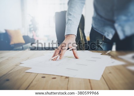 Businessman at work. Holding pencil in his hand. Architectural project on table. Blurred background, horizontal mockup.