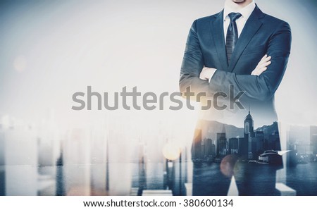 Young businessman wearing modern suit and standing with his arms crossed. Double exposure. Horizontal, contemporary city background
