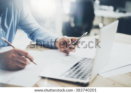 Businessman in workplace. Texting message smartphone and holding pencil hands. Generic design notebook wood table. Horizontal mockup, blurred background