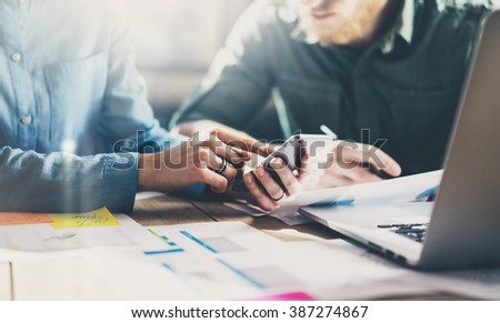 Business meeting concept. Photo young businessmans crew working with new startup project in modern loft. Generic design smartphone holding female hands. Horizontal, film effect