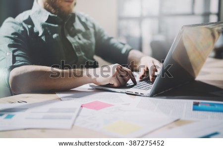 Photo bearded designer working with new project. Generic design notebook on wood table.  Analyze plans, papers, hands keyboard. Blurred background, film effect