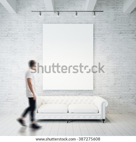Photo of man in gallery. Waching empty canvas hanging on the brick wall and vintage classic sofa wood floor. Square, blank mockup. Motion blur