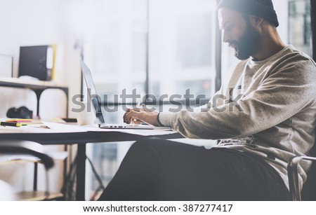 Photo bearded graphic designer working with new project modern loft. Generic design notebook on wood table.  Analyze plans, papers, hands keyboard. Blurred background, film effect