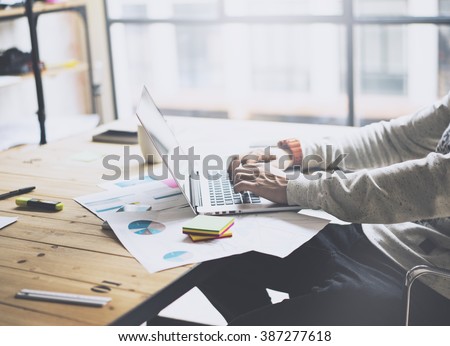 Photo bearded businessman working with new project modern loft. Generic design notebook on wood table.  Analyze plans, papers, hands texting keyboard. Blurred background, film effect