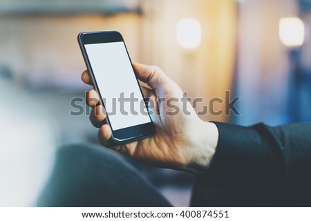 Photo banker relaxing in modern loft office.Man sitting chair night.Using contemporary smartphone,blurred background.Blank screen ready for your business information.Horizontal,film effect.