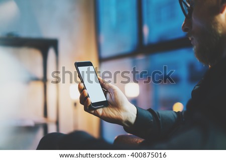 Photo businessman relaxing modern loft office.Man sitting chair night.Using contemporary smartphone,blurred background.Blank screen ready for your business information.Horizontal,film effect.