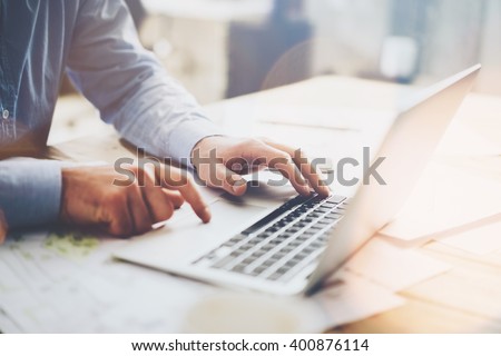Photo businessman working on modern loft office. Man sitting wood table and using contemporary notebook, texting message keyboard. Horizontal, film, flare effect