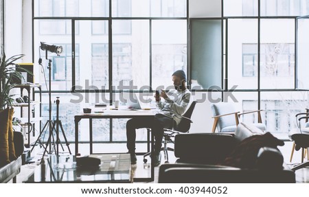 Photo bearded account manager working with new project oped space loft studio. Looking modern smartphone. Contemporary laptop on wood table. Creative process.Blurred background, film effect