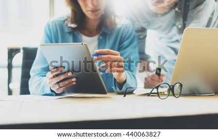 Coworkers team brainstorming process modern design studio.Project producer reading report tablet,glasses wood table.Young business crew working with startup.Using digital devices. Blurred,film effect