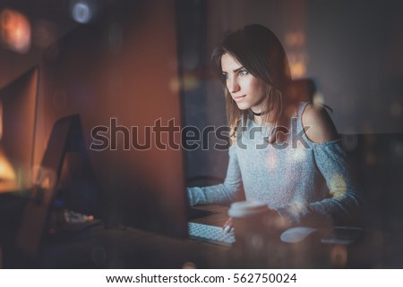 Attractive young woman working on coworking office at night. Girl using contemporary desktop computer, blurred background. Horizontal, film effect, reflections