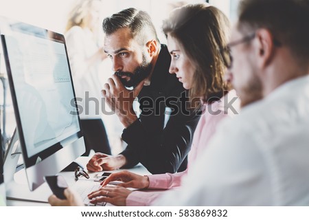 Teamwork concept.Young creative coworkers working with new startup project in modern office.Group of three people analyze data on desktop computer.Horizontal,blurred background
