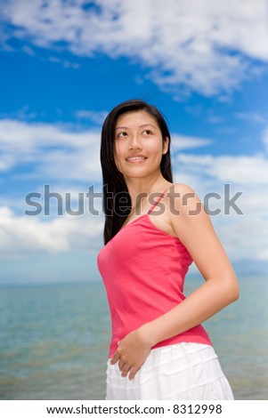 woman smiling looking far with red top and white skirt stand by the sea