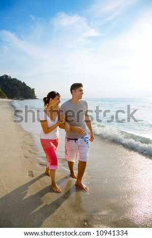 happy asian couple walking along the beach
