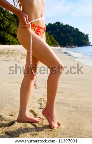 healthy woman measuring slim body figure on the beach in bikini