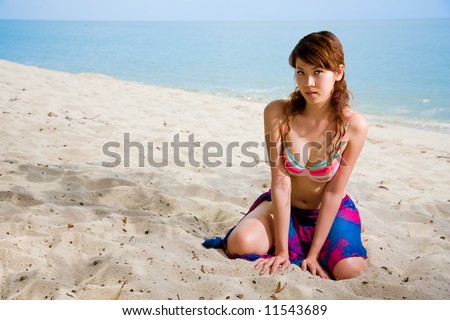 sexy looking asian woman in bikini, kneeling on the beach