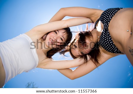 two young happy girls fooling around looking down with sun and blue sky behind