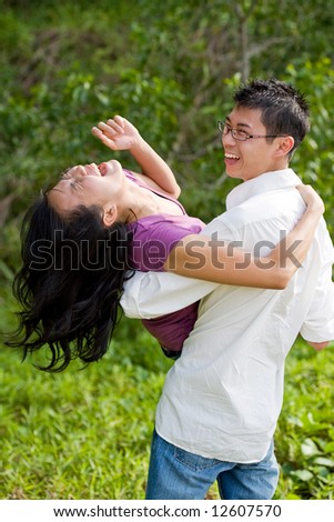 happy young asian couple having fun with the guy carrying the girl