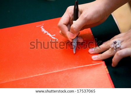hand of a guest holding a pen writing on a red chinese wedding guests book