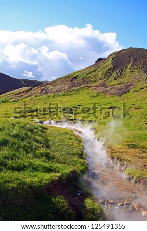 Geothermal bathing river with green grass and blue sky, Reykjadalur near Hengill volcano, Iceland