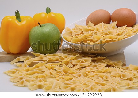 some pasta on white bowl, eggs, apple,and yellow paprikas
