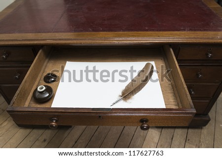 Vintage set with quill and ink pot on top of parchment paper inside writing desk drawer.