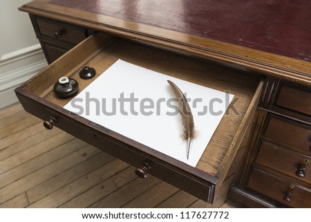 Vintage set with quill and ink pot on top of parchment paper inside writing desk drawer.