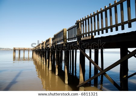 Wooden pier over brown water with blue sky and mountains far away in the background.