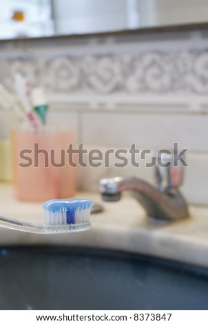 Detail shot of a tooth brush with tooth paste on it and basin in the blurred background