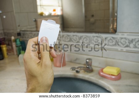 Detail shot of a male hand holding a blank dental floss box, with basin in the blurred background.