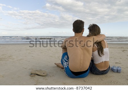 Young healthy couple sited in the sand, looking out into the sea.