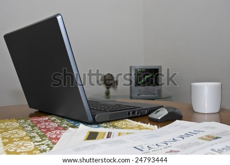 Low angle shot of laptop with TV screen showing rising stock graphic.