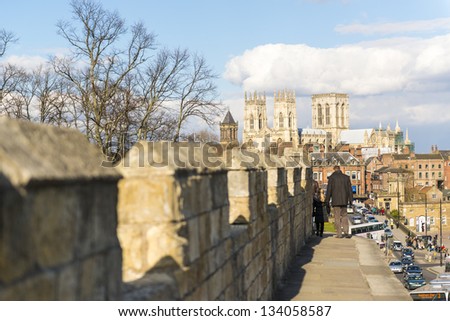 YORK, UK - MARCH 30: Pedestrians walking on the medieval wall that surrounds the city, with York Minster in the background. March 30, 2013 in York.