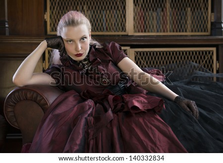 Beautiful caucasian woman in red Victorian dress waiting in old library