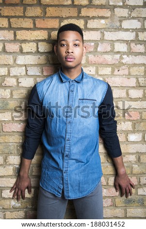 Portrait of handsome dark skinned male model wearing casual clothes against brick wall