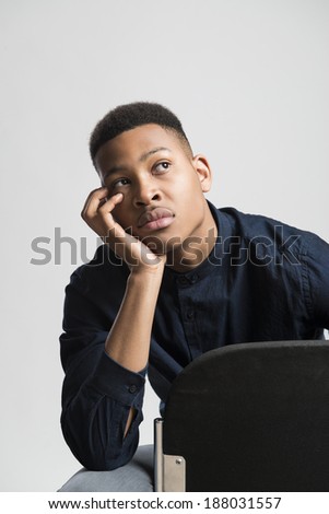 Portrait of handsome dark skinned male model holding head on hand and wearing casual clothes against white background