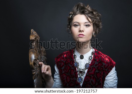 Portrait of beautiful Caucasian model in red Victorian-style velvet dress, seated on wooden chair