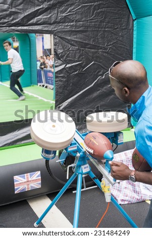 LONDON UK - SEPTEMBER 27: Man using launcher to throw American football ball to receiver in Regent St. September 27 2014 in London. The street was closed to host NFL related games and events.