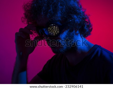 Cyborg man in shadows with red backdrop and blue key light, with bionic led eye