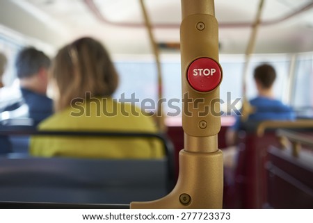 Detail of red stop button inside double decker bus in London, UK, with passengers seated in the blurred background.