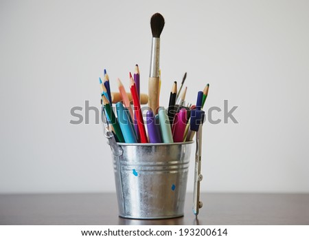 Various pencils, pens, and colored markers in a shiny metal bucket, white iso. bucket of markers.