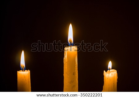 Three burning wax candles on a black background