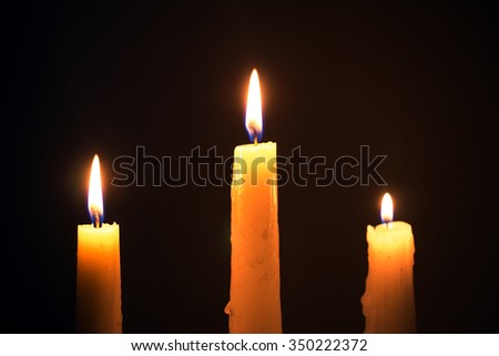 Three burning wax candles on a black background. religion