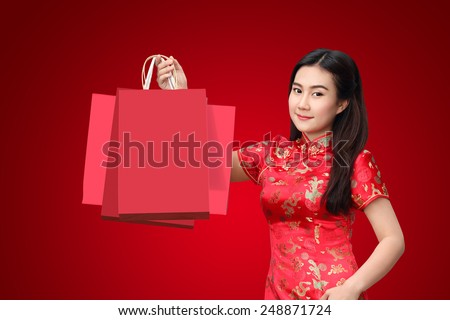 Chinese beautiful asian woman dress traditional cheongsam holding red shopping bag isolated on red background, Happy chinese new year