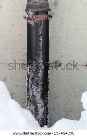 The old drain pipe with frozen water in a snowdrift