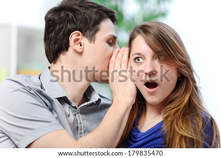 man whispering in the ear of his surprised wife